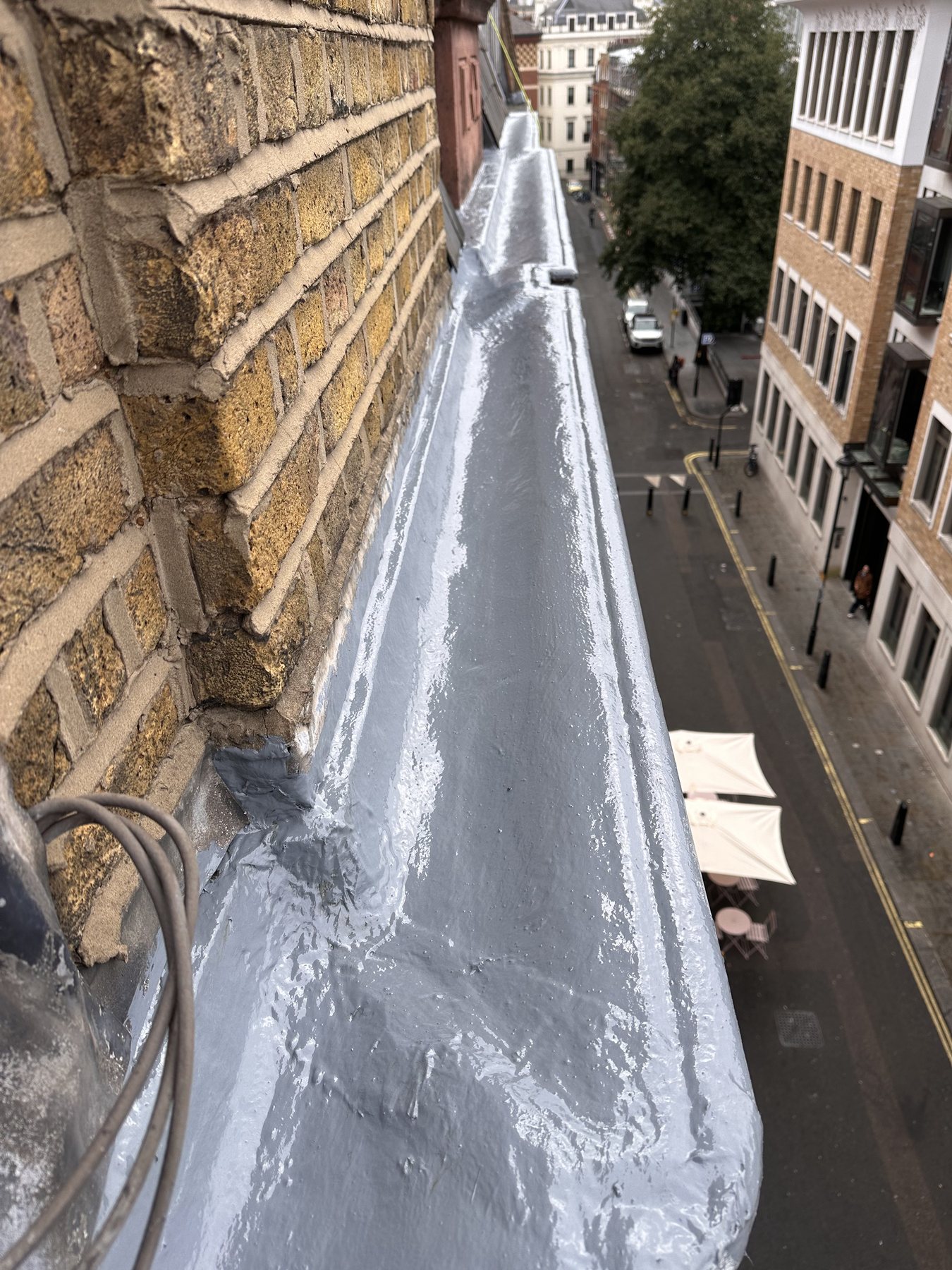 Rope access roof repair work in London on a high level roof edge finished with grey waterproof coating
